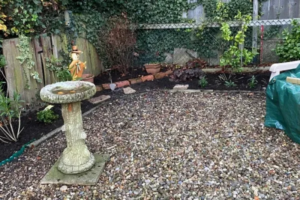 A graveled area with a bird bath, having had leaves cleared away