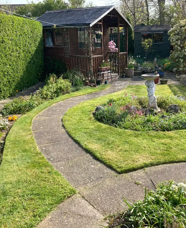 A garden path that winds its way through tidy grass to a summer house